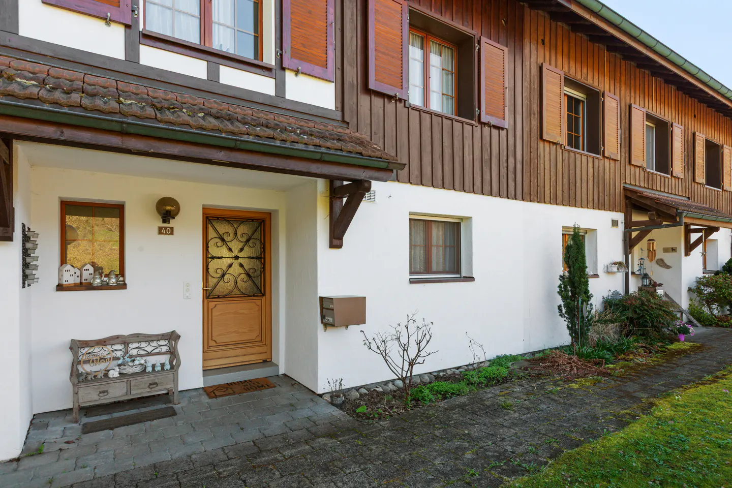 Exterior view of a row of townhouses with white walls, brown wood trim, and red shutters. A stone walkway leads to the front doors.