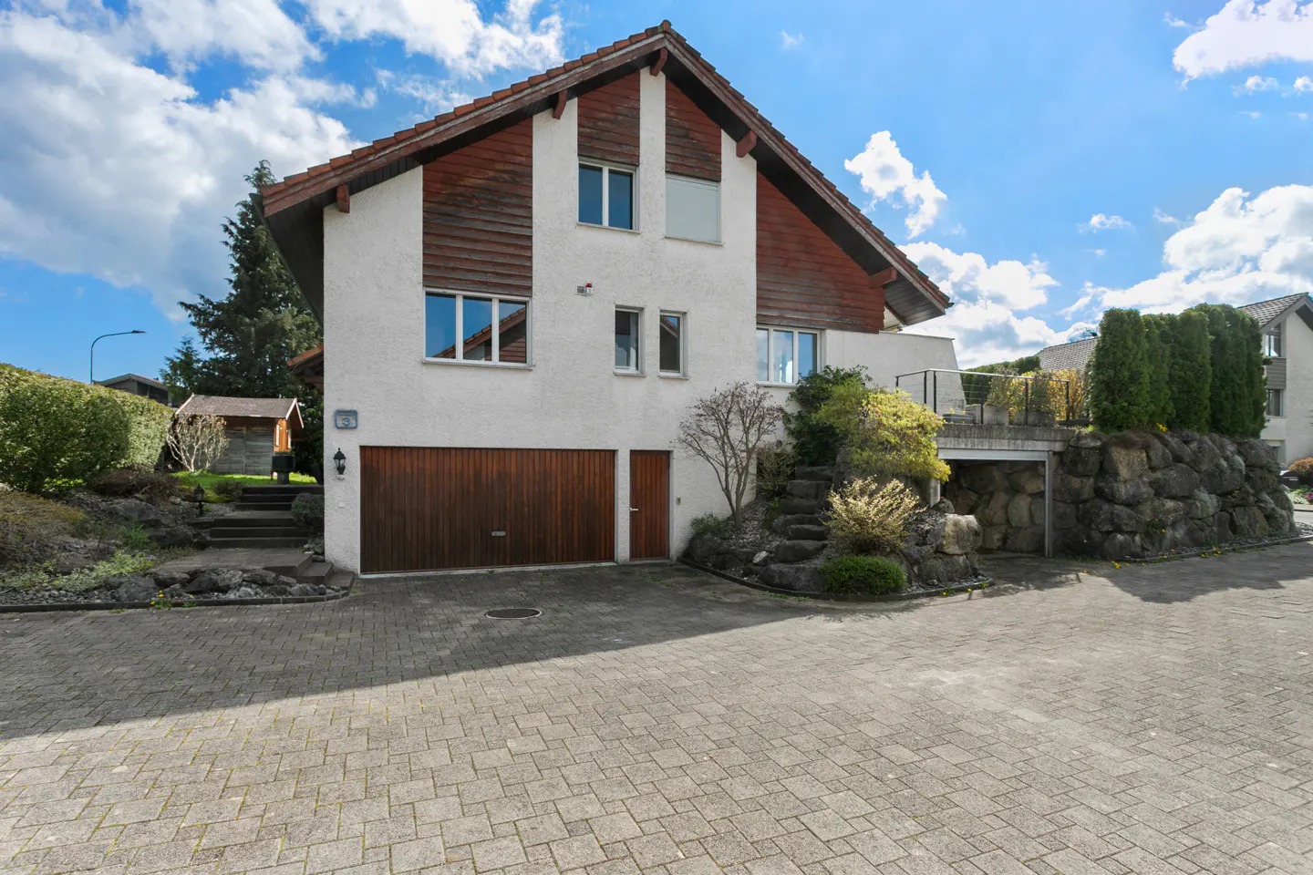 Exterior view of a two-story white house with a brown roof and garage door on a paved driveway.