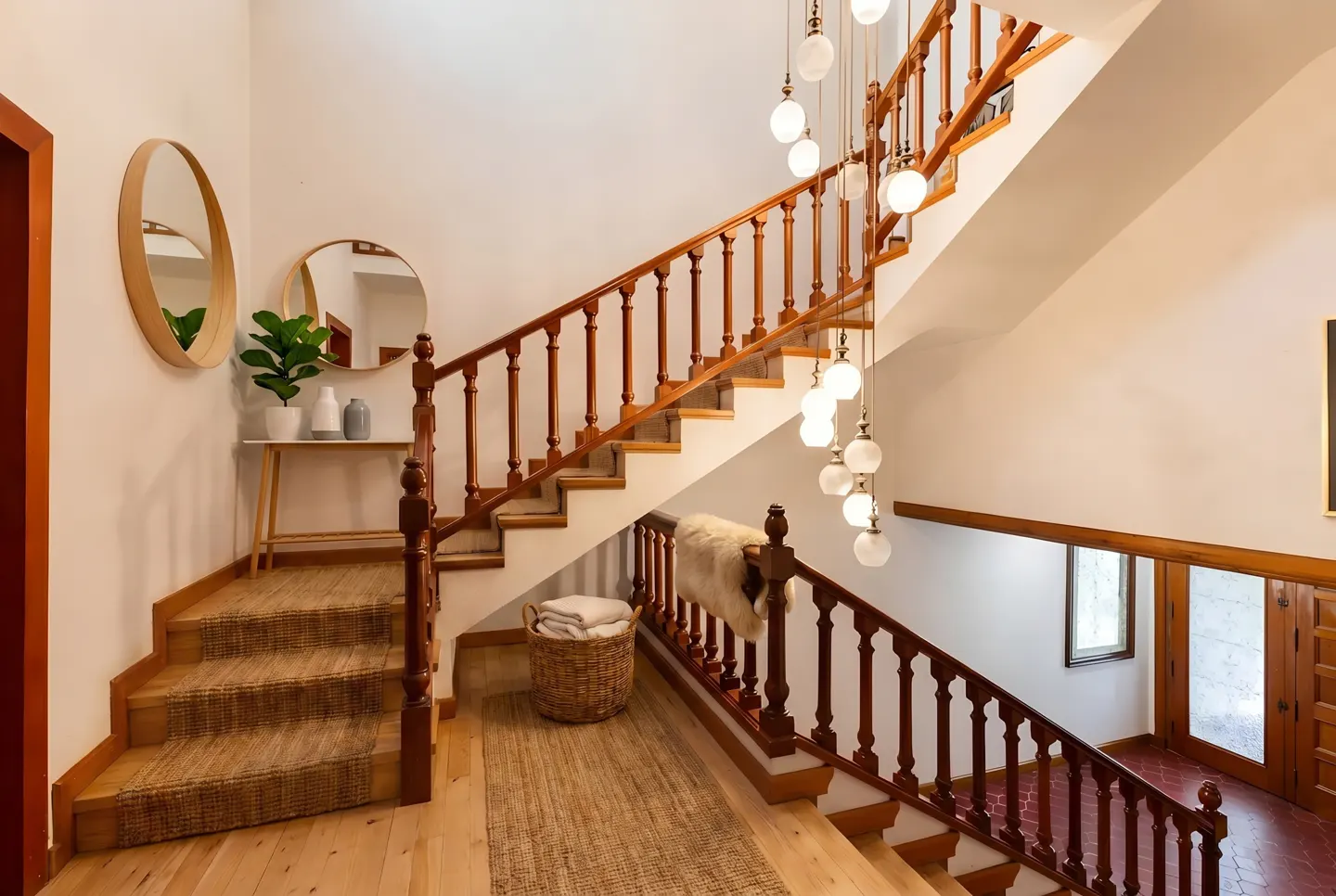 Interior view of a staircase with wooden banister, jute runner, and globe pendant lights in a white-walled home.