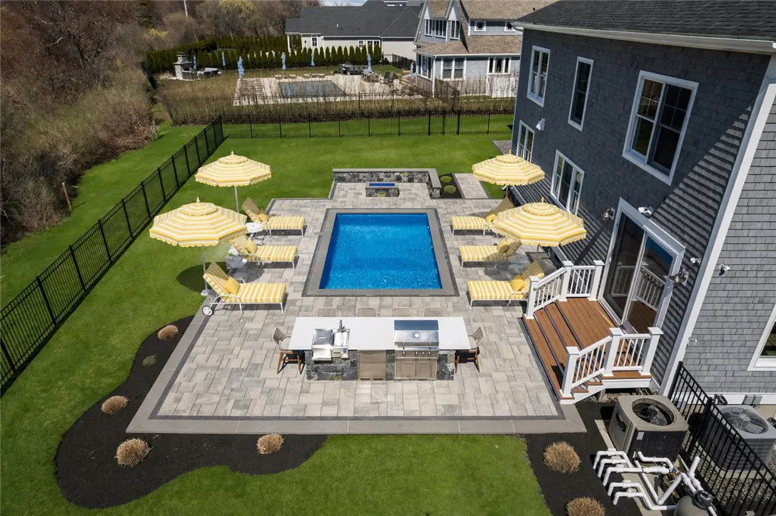 Aerial view of a backyard with a pool, patio, outdoor kitchen, lounge chairs, and yellow striped umbrellas.