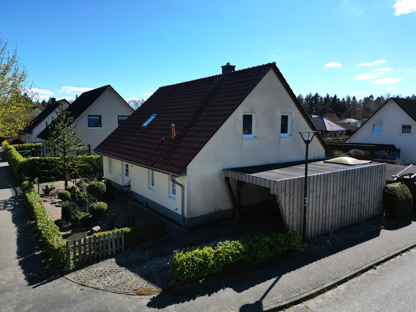 A cream-colored house with a brown roof and a wooden carport on a sunny day.