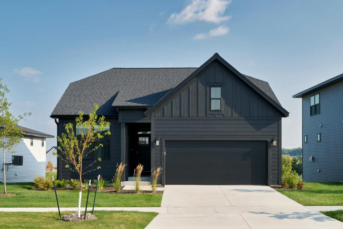 A modern, one-story house with dark gray siding, a gray roof, and a two-car garage on a sunny day.