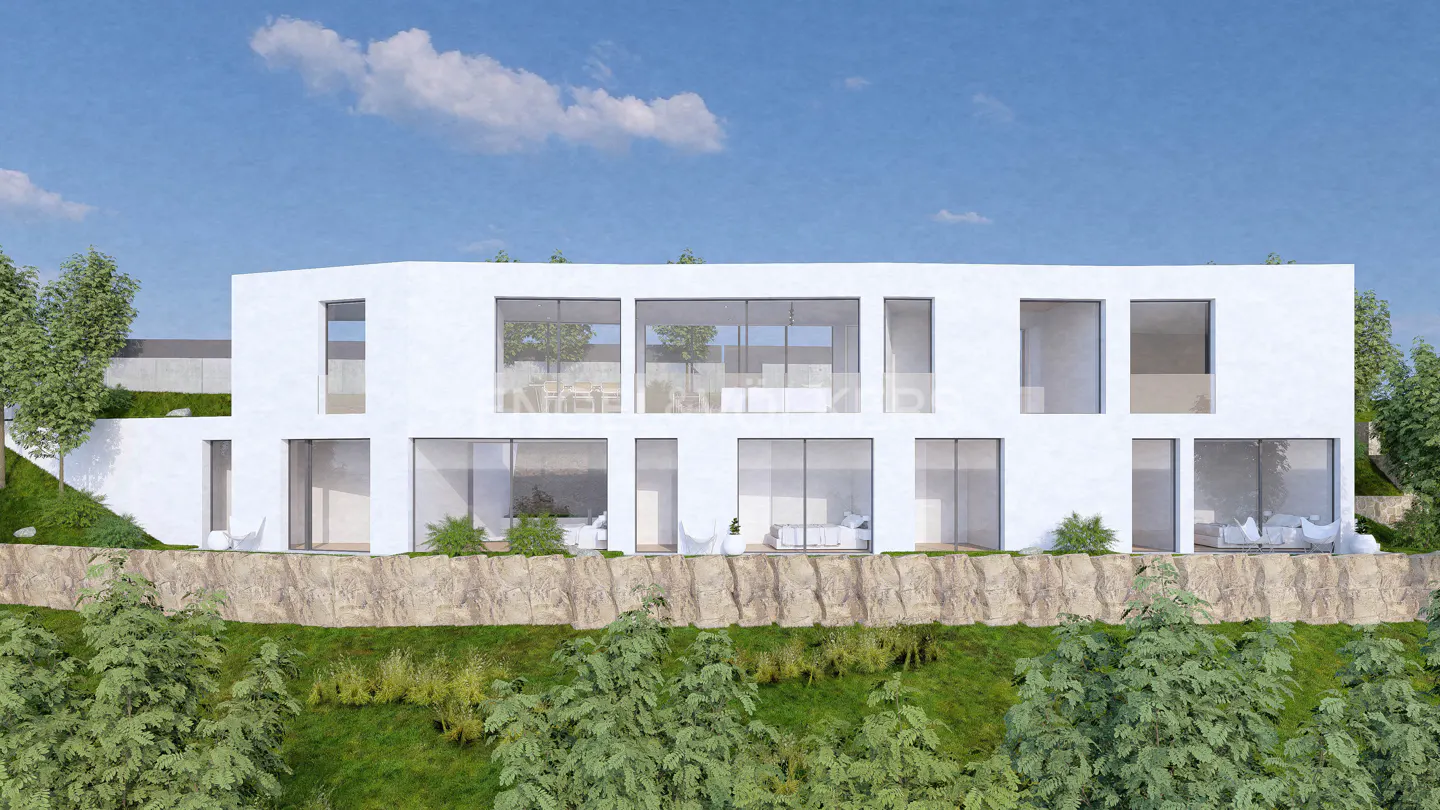 Modern white house with large windows on a rocky hill, surrounded by green trees and a blue sky with white clouds.