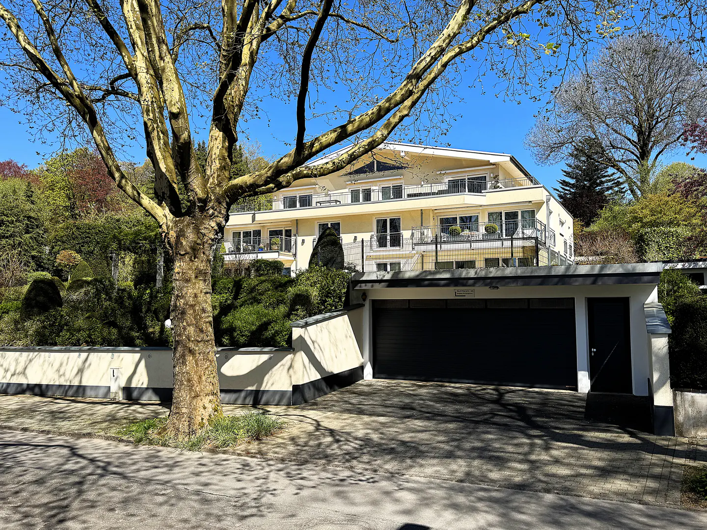 Exterior view of a three-story yellow building with balconies, a black garage door, and a tree in the foreground.