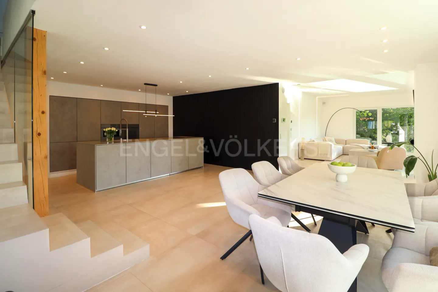 Modern open-plan kitchen and dining area with a marble table, light-colored chairs, and a sleek gray kitchen island.