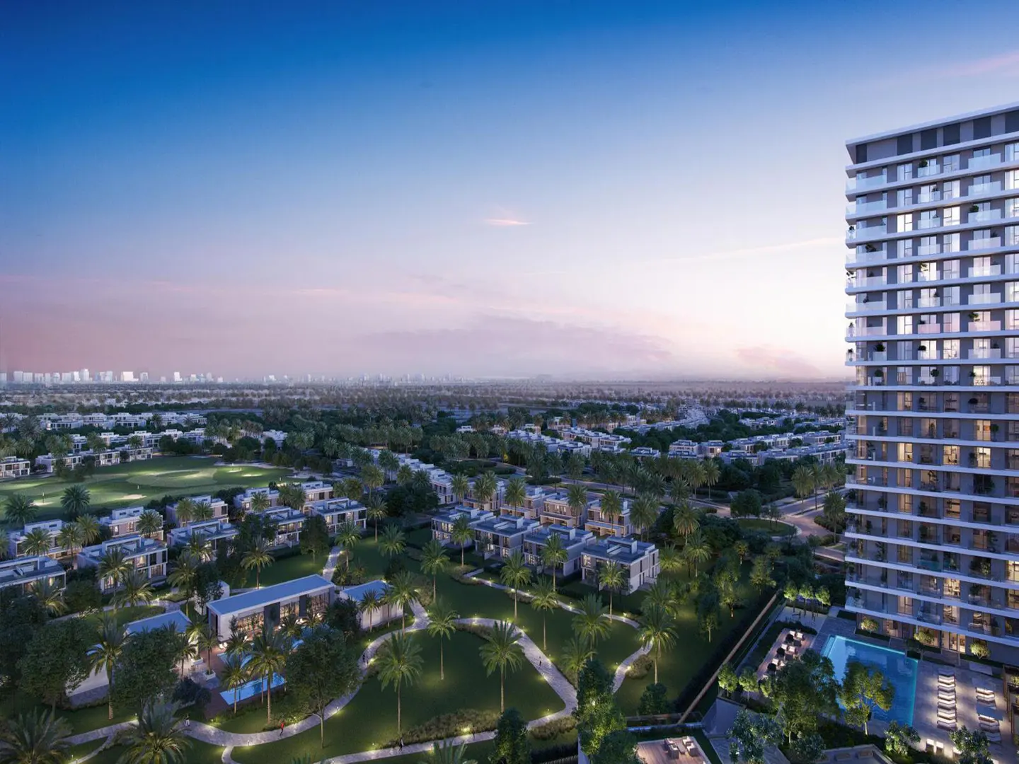 Aerial view of a modern residential area with a tall apartment building, villas, green spaces, and a distant city skyline under a blue and pink sky.