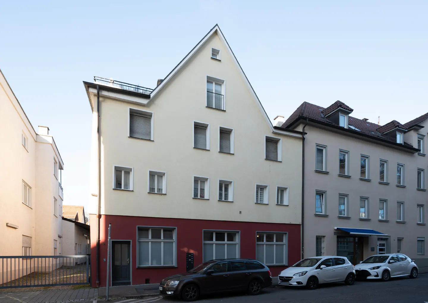 A three-story building with a red base and cream-colored upper floors, parked cars in front.