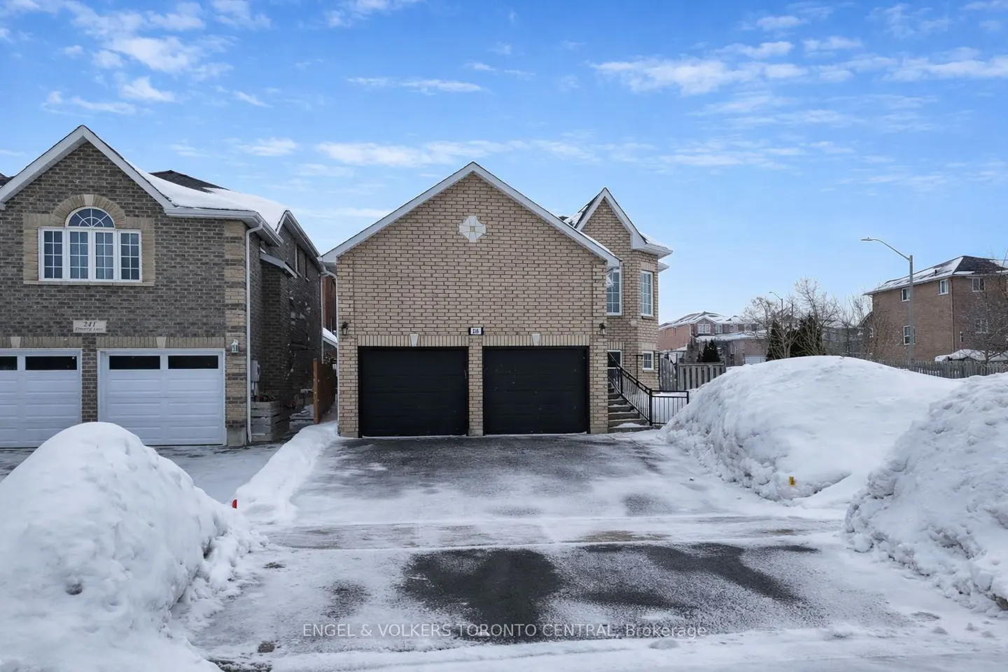 Two-story brick house with black garage doors and snow-covered driveway on a sunny winter day.