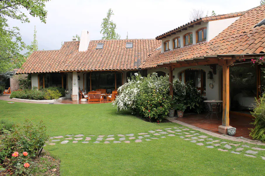 Exterior view of a house with a red tile roof, green lawn, stone pathway, and patio furniture.