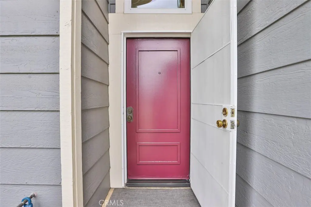 A partially open white door reveals a maroon front door with a peephole, set against gray siding.