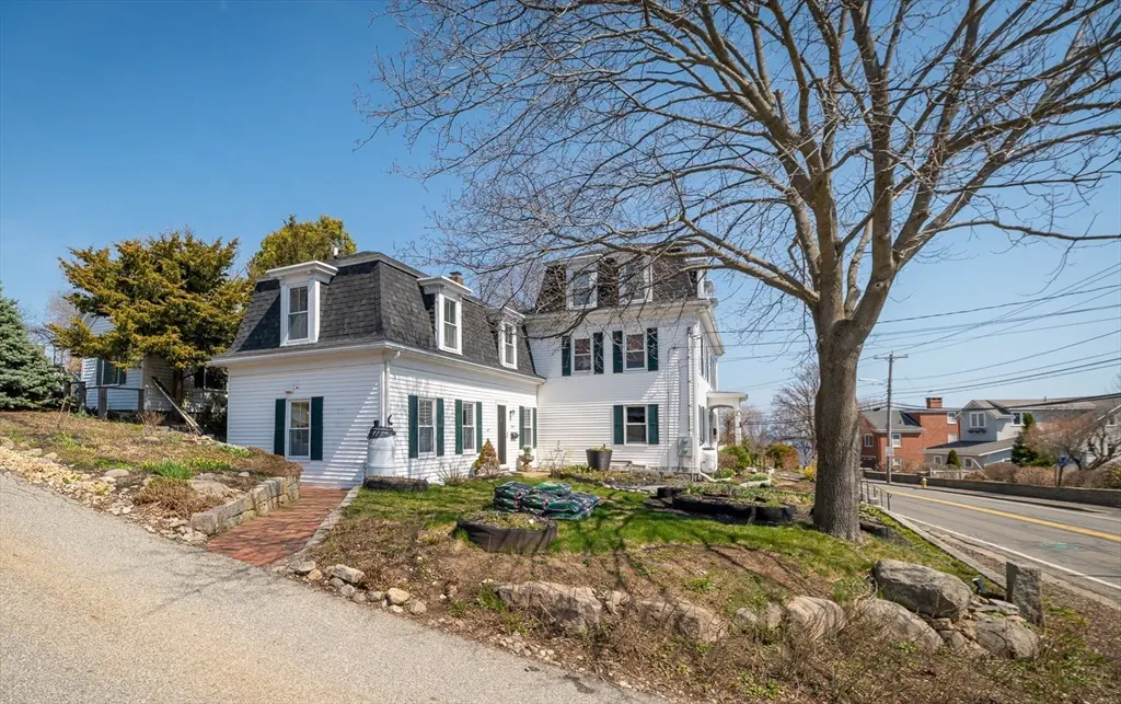 Exterior view of a two-story white house with green shutters and a black roof on a sunny day.