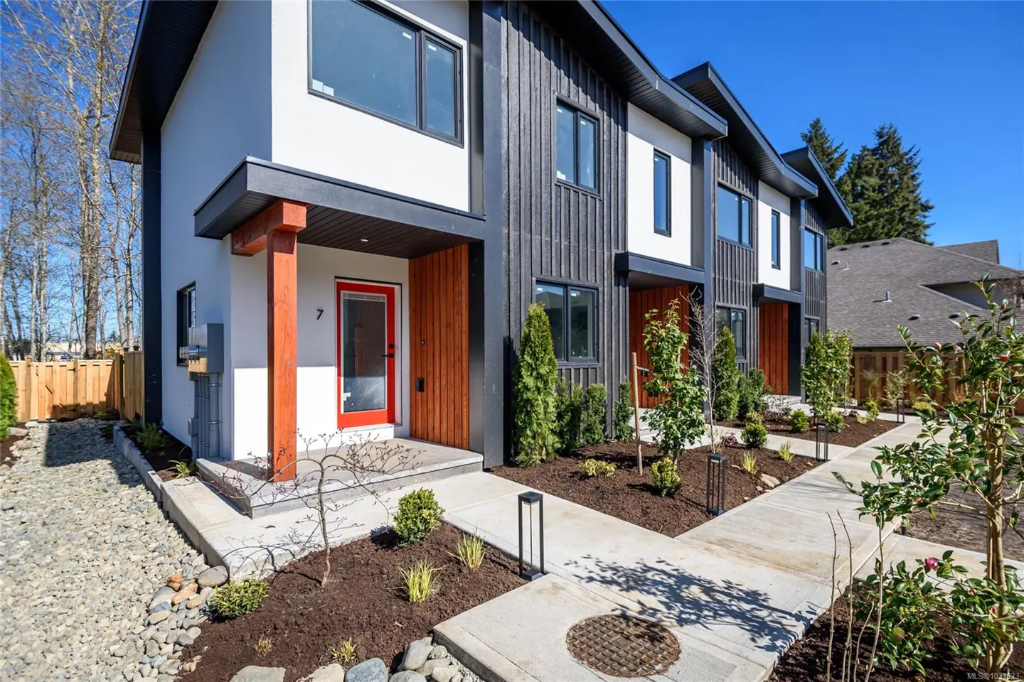 Modern townhouses with white and dark gray siding, red doors, and landscaped yards under a blue sky.