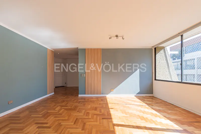 Empty room with herringbone wood floors, blue-gray walls, and a large window with sunlight streaming in.