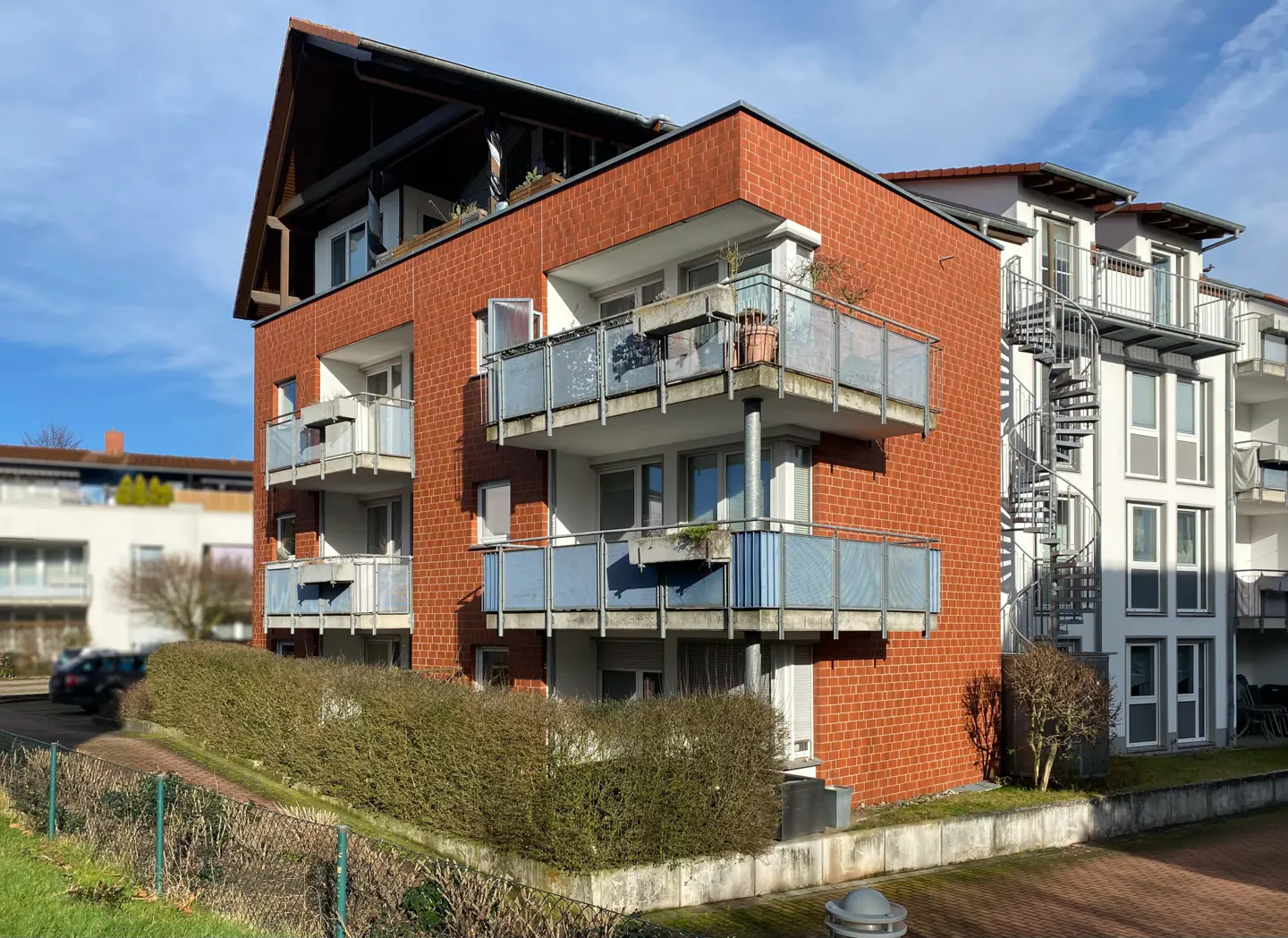 Exterior view of a red brick apartment building with balconies and a spiral staircase.