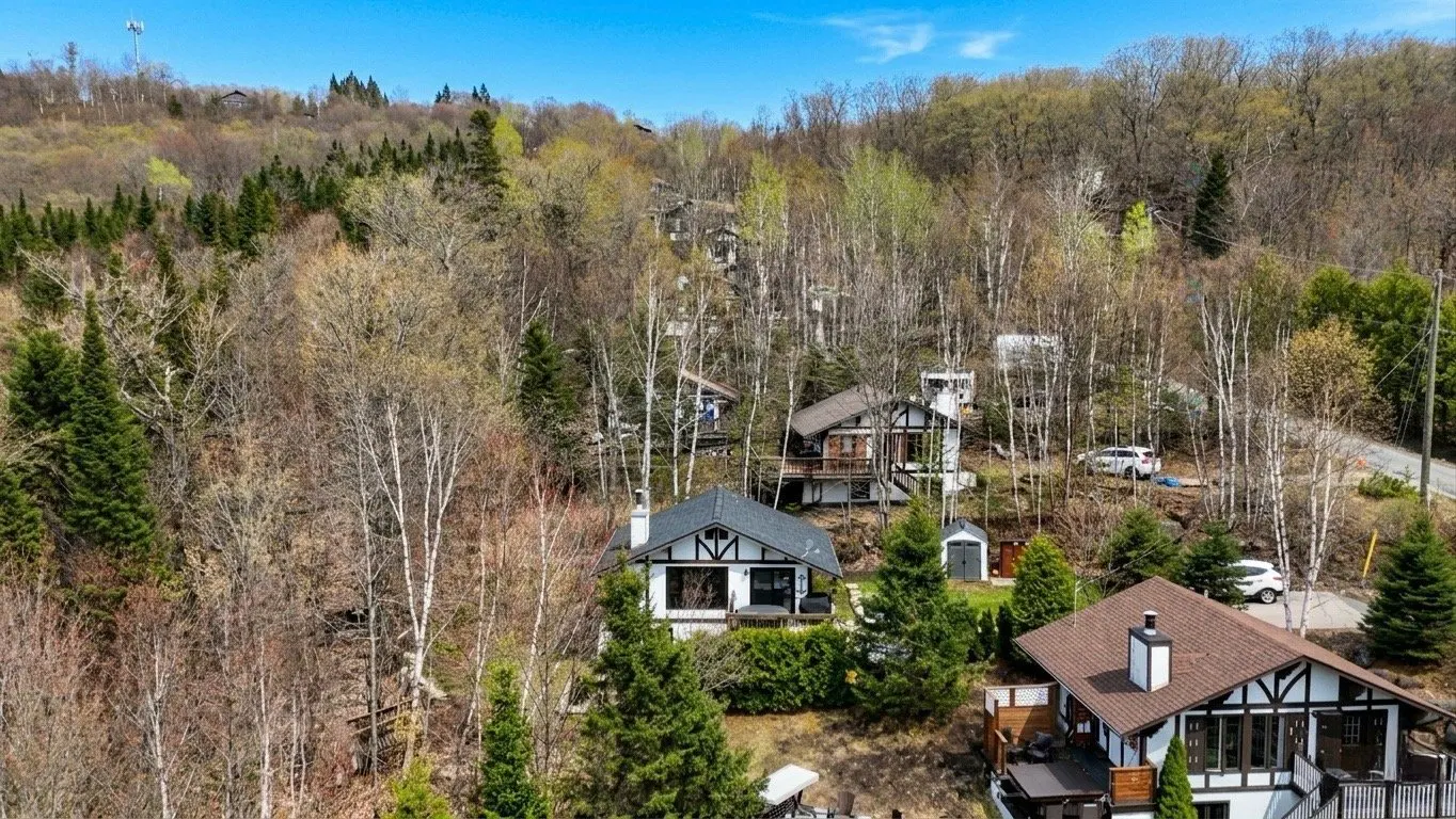 Scenic view of Tudor-style homes nestled among trees on a hillside under a blue sky.