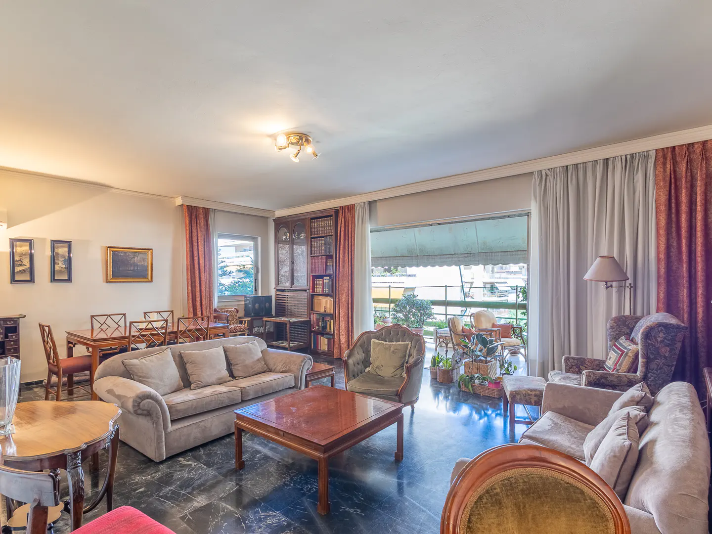 Spacious living room with marble floors, beige sofas, wooden coffee table, dining area, and a balcony with sheer curtains.