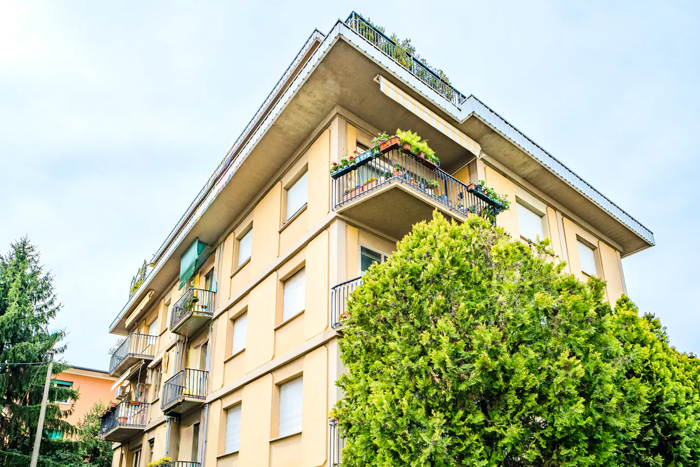 A low-angle view of a tan apartment building with black balconies and green plants.