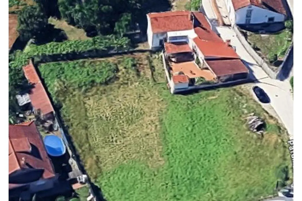 Aerial view of a grassy lot bordered by houses with red roofs and green trees.