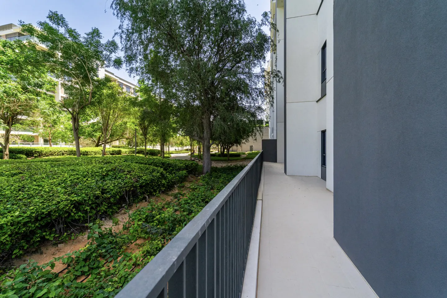 Apartment complex with a gray metal railing, a walkway, and green landscaping with trees.