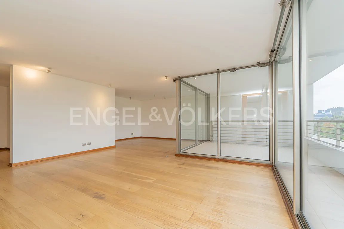 Empty room with light wood floors, white walls, and floor-to-ceiling glass doors leading to a balcony. Engel & Völkers logo on the wall.