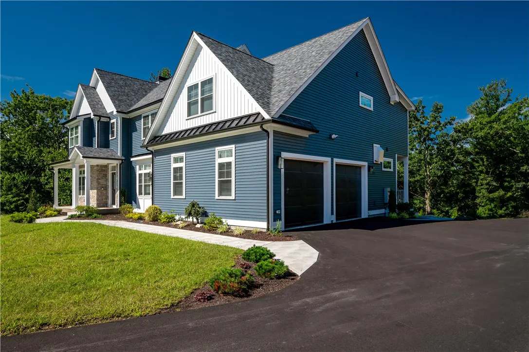 Two-story blue house with white trim, gray roof, and black garage doors on a sunny day.