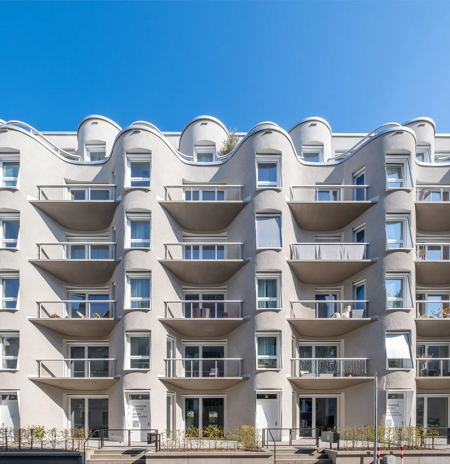 Modern apartment building with curved facade and balconies under a clear blue sky.