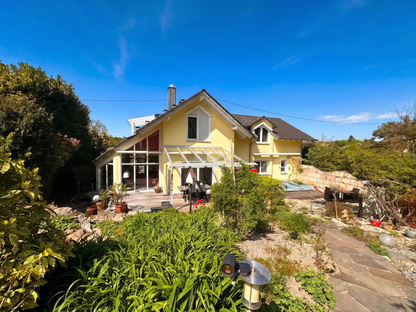 Exterior view of a yellow two-story house with a brown roof, surrounded by lush greenery and a blue sky.