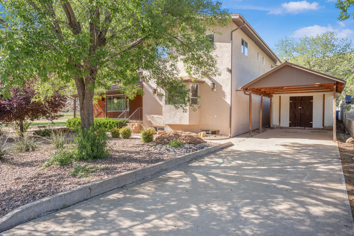 Two-story beige house with a brown carport and a concrete driveway on a sunny day.
