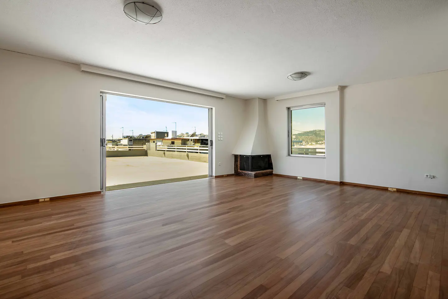 Bright, empty room with hardwood floors, white walls, and a fireplace. Sliding glass doors open to a rooftop patio with city views.