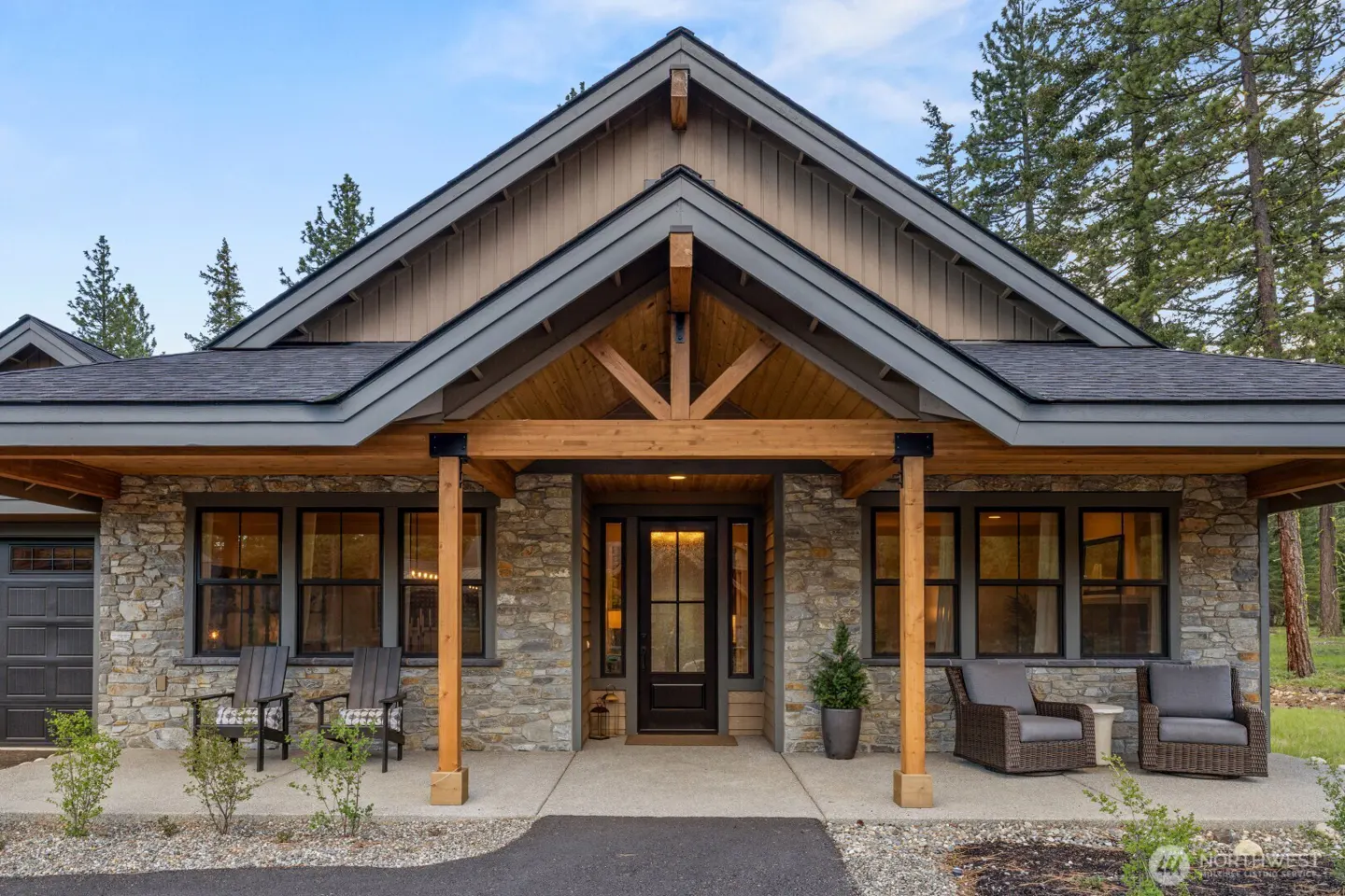 Stone house exterior with a covered porch, wooden beams, and outdoor seating. The roof is dark gray.