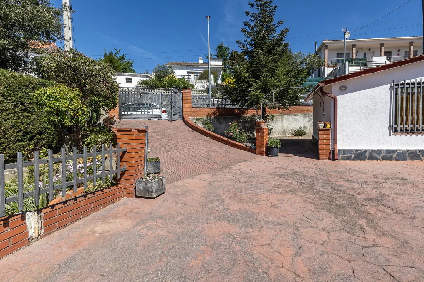 Exterior view of a house with a red brick driveway, a white house, and a metal gate.