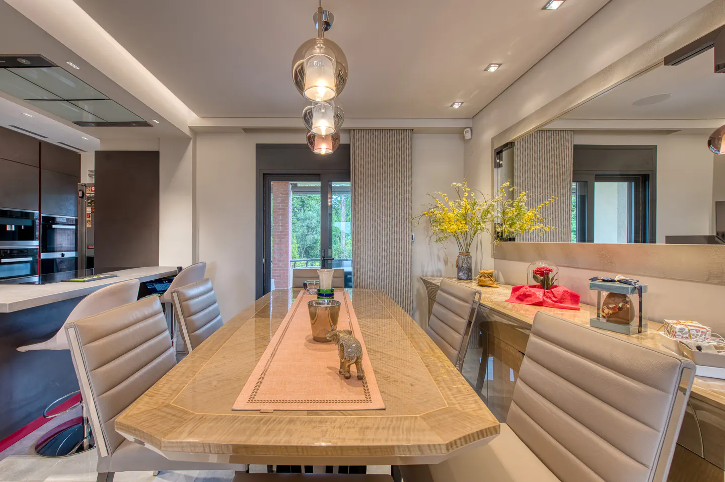 Modern dining room with a wooden table, beige leather chairs, pendant lights, and a large mirror reflecting the space.