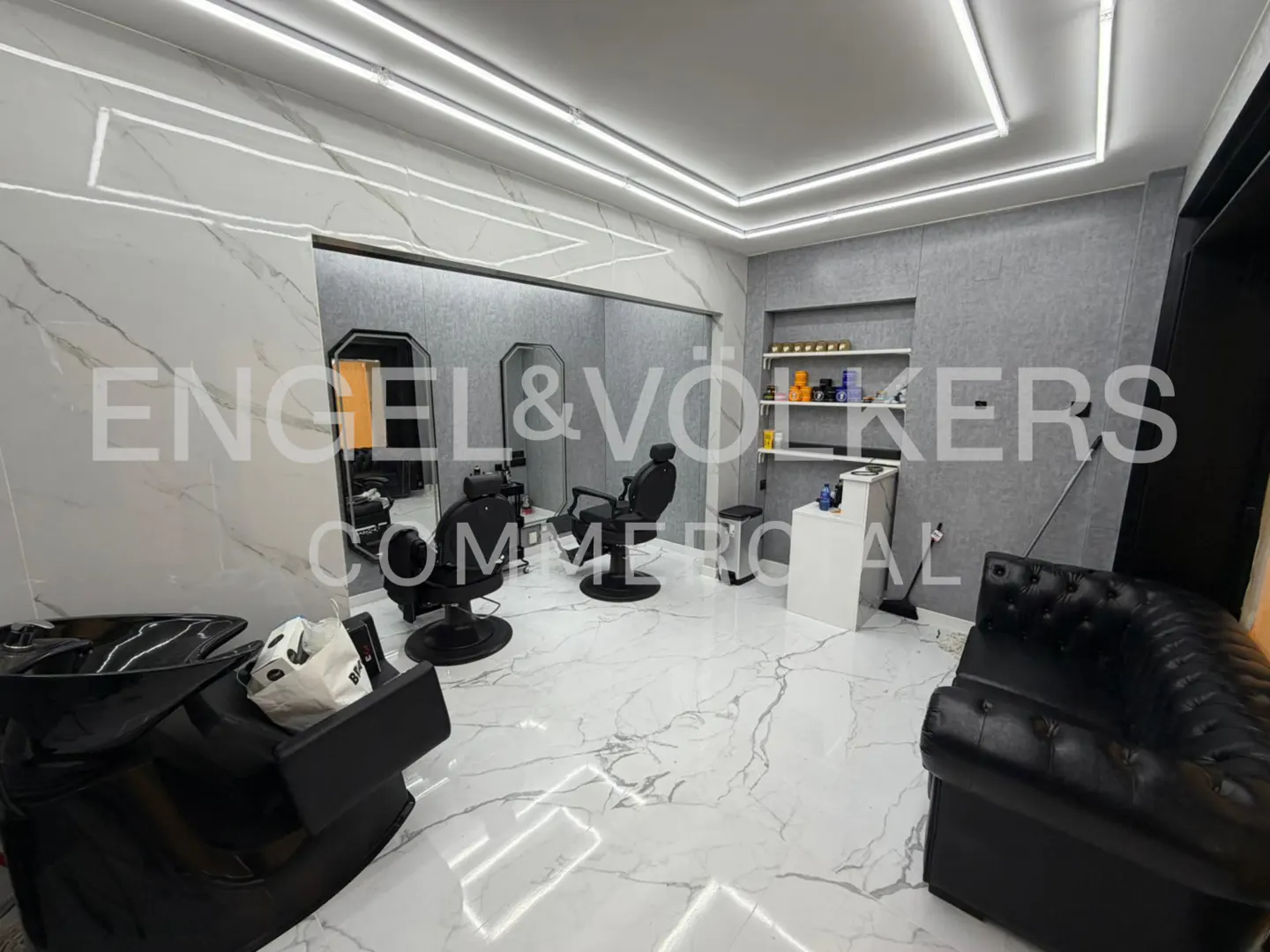 A modern barber shop with black chairs, mirrors, and a black leather sofa against a marble wall.