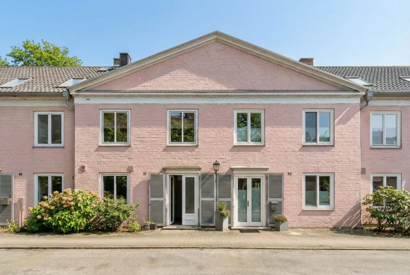 A two-story pink brick townhouse with white trim, gray shutters, and a gray tiled roof.