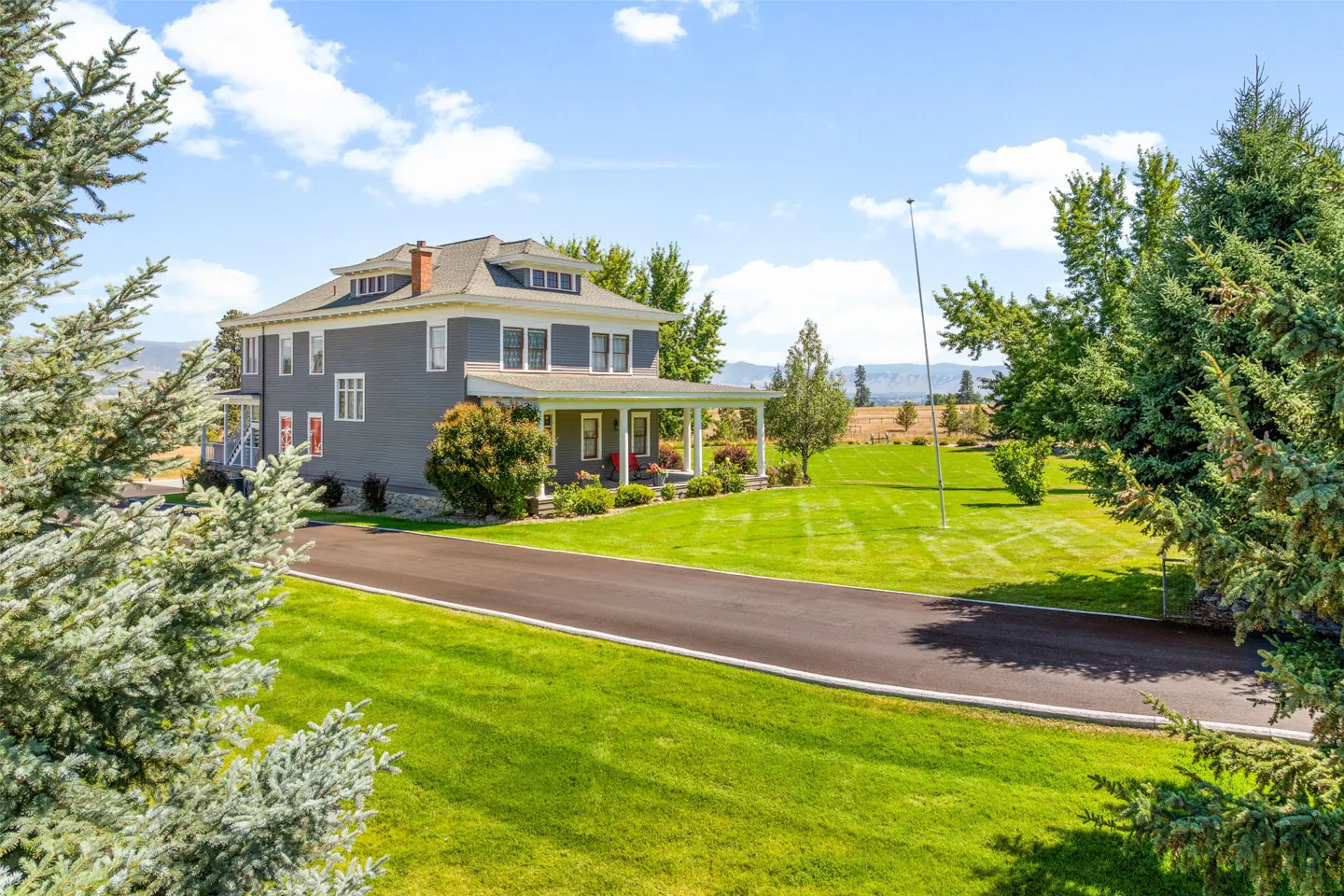 Two-story gray house with white trim, a covered porch, and a large green lawn on a sunny day.