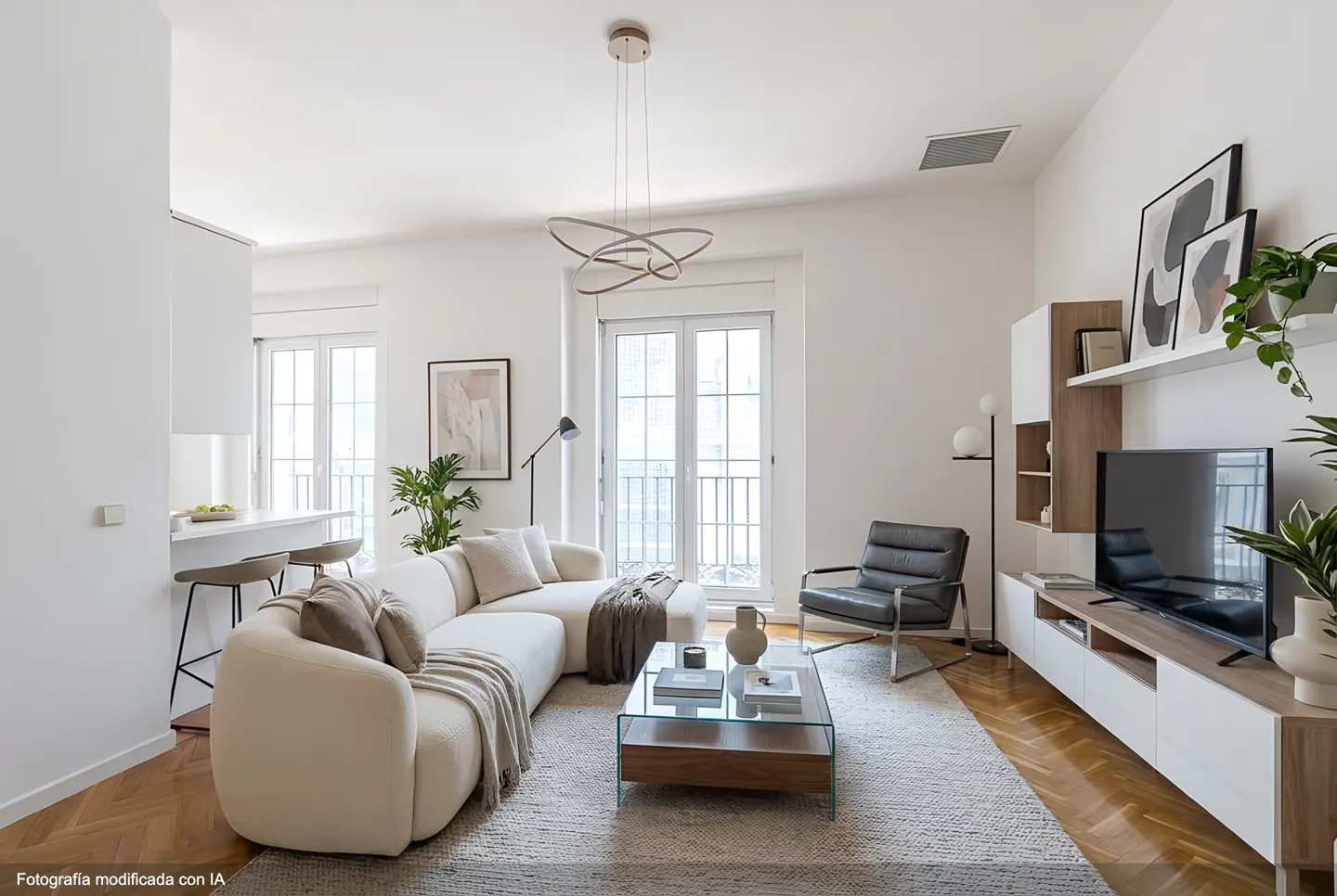 Bright living room with white walls, a cream sectional sofa, glass coffee table, and a black leather chair on a herringbone wood floor.