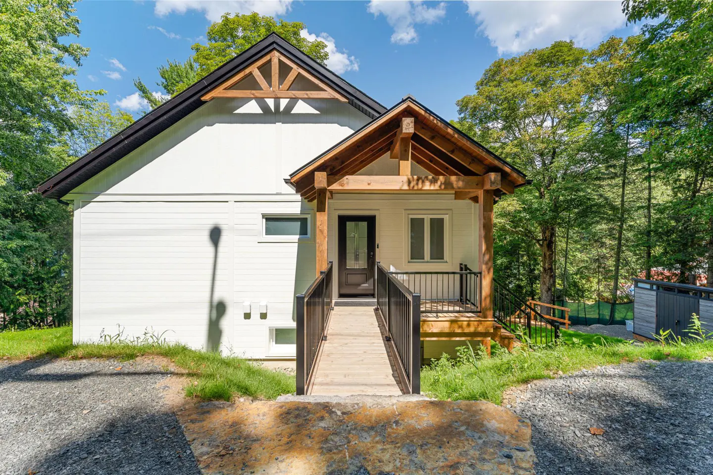 Exterior of a white house with a black roof and a wooden porch with a ramp.