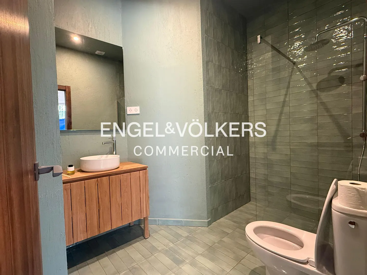 Bathroom with green walls and floor tiles, wood vanity with white sink, toilet, and shower.