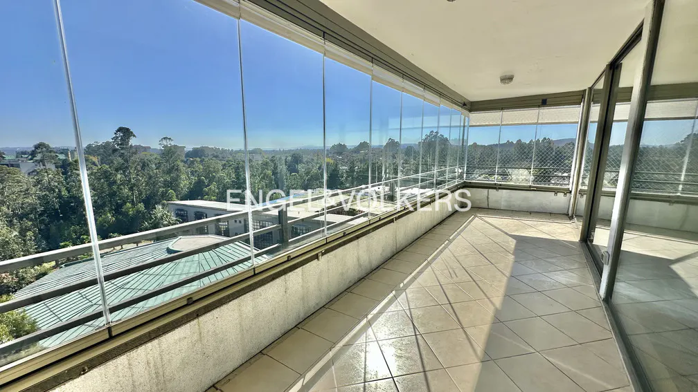 A bright balcony with glass walls overlooks a lush green landscape under a clear blue sky.