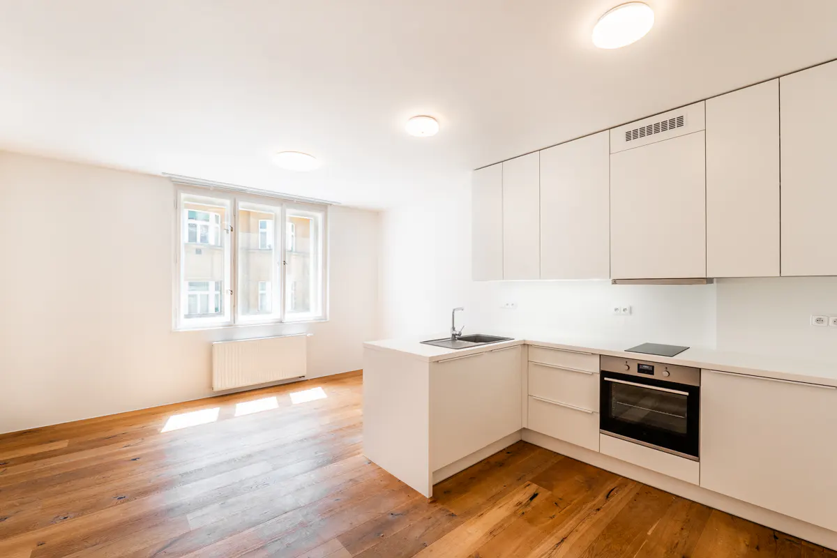 Bright, modern kitchen with white cabinets, countertops, and wood floors. A large window lets in natural light.
