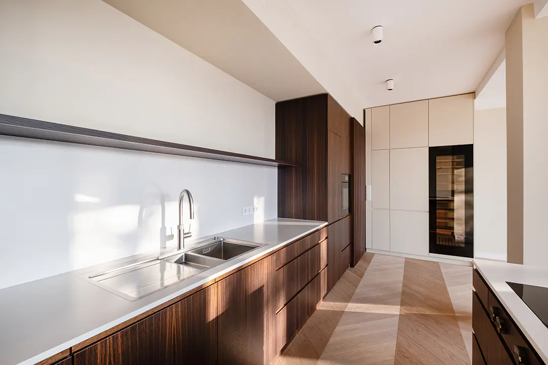 A modern kitchen with dark wood cabinets, a stainless steel sink, and a light wood floor in a herringbone pattern.