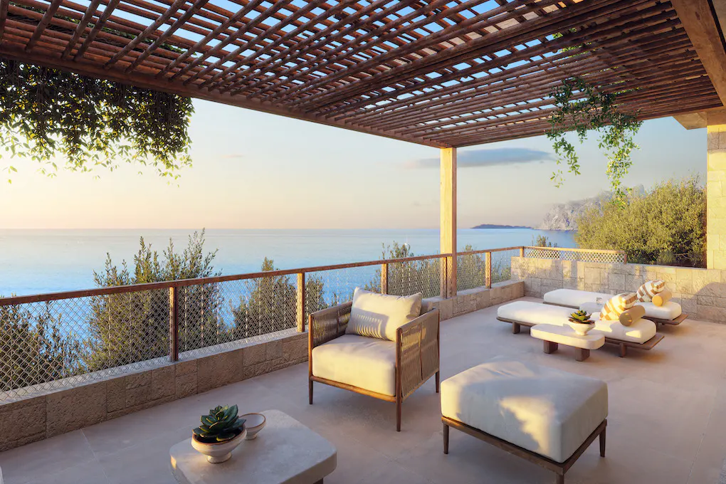 Outdoor patio with a wooden pergola, lounge chairs, and ocean view. The patio has stone walls and a metal railing.