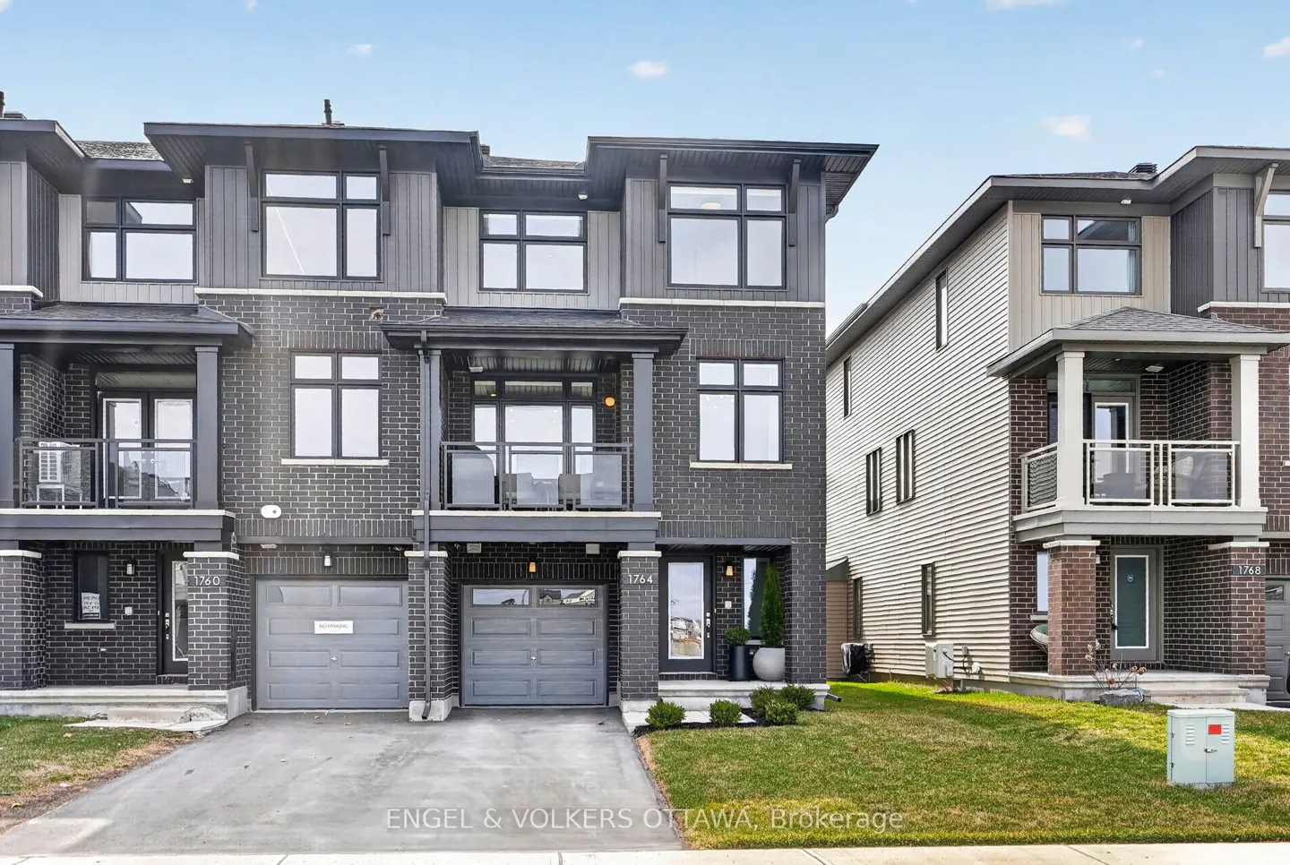 Modern three-story townhouses with gray brick and siding, black trim, and attached garages on a sunny day.