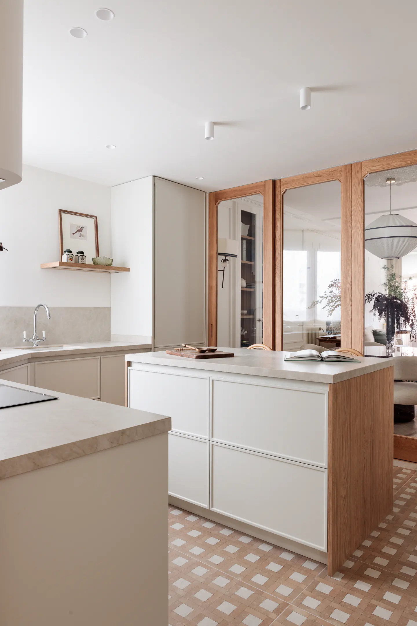 Bright kitchen with white cabinets, a large island, and light wood accents. A book rests on the island's countertop. Tiled floor.