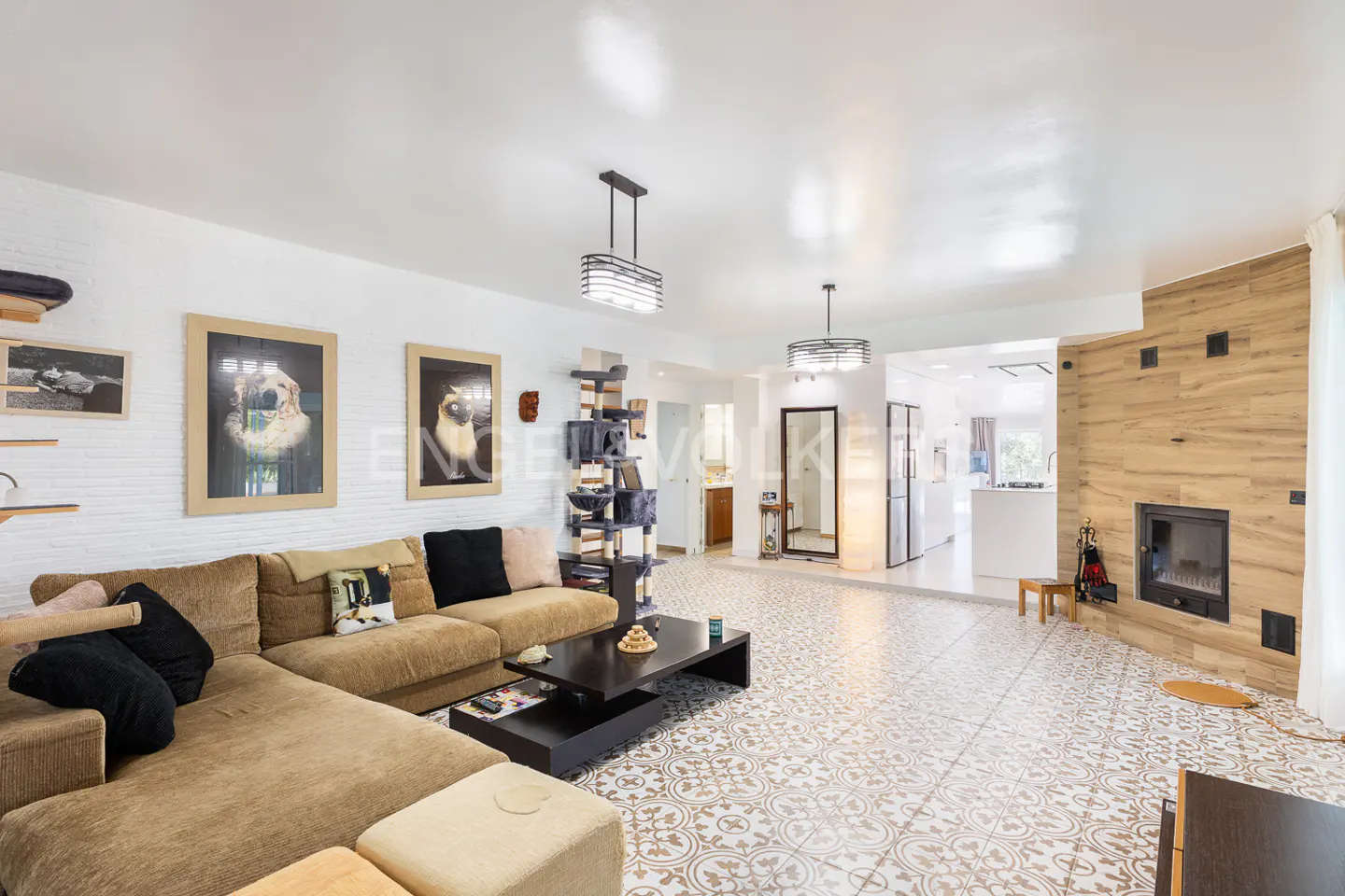 A living room with a brown sectional sofa, a black coffee table, and patterned tile flooring. A fireplace and cat tree are also visible.