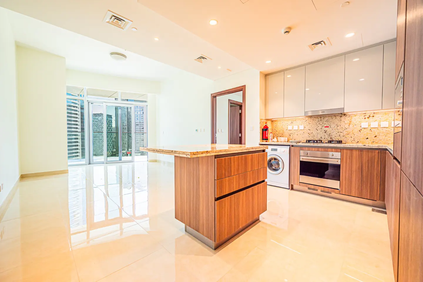 Bright, modern apartment interior with a kitchen island, white cabinets, and a balcony with city views.