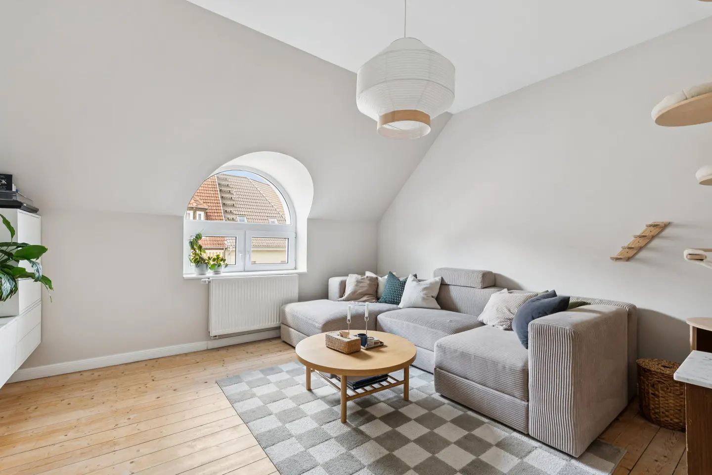 Bright living room with a gray sectional sofa, round wood table on a gray and white checkered rug. Arched window and wood floors.