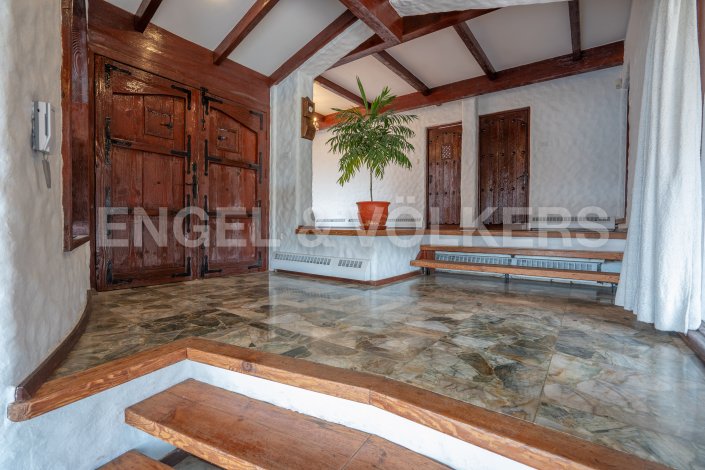 Interior view of a home's foyer with marble floors, wooden doors, and a potted plant. The walls are white and textured, and the ceiling has exposed wooden beams. [AI-generated text]