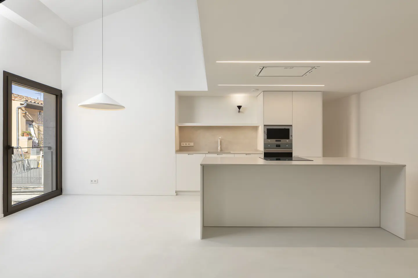 Bright, modern kitchen with white walls, cabinets, and floors. A large island sits in the center, and a door leads to a balcony.