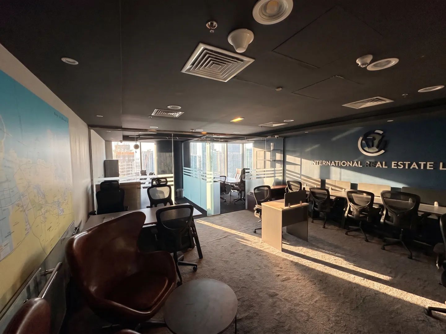 Office space with desks, chairs, and a map on the wall. Natural light streams in from the windows. "International Real Estate" logo on the wall.